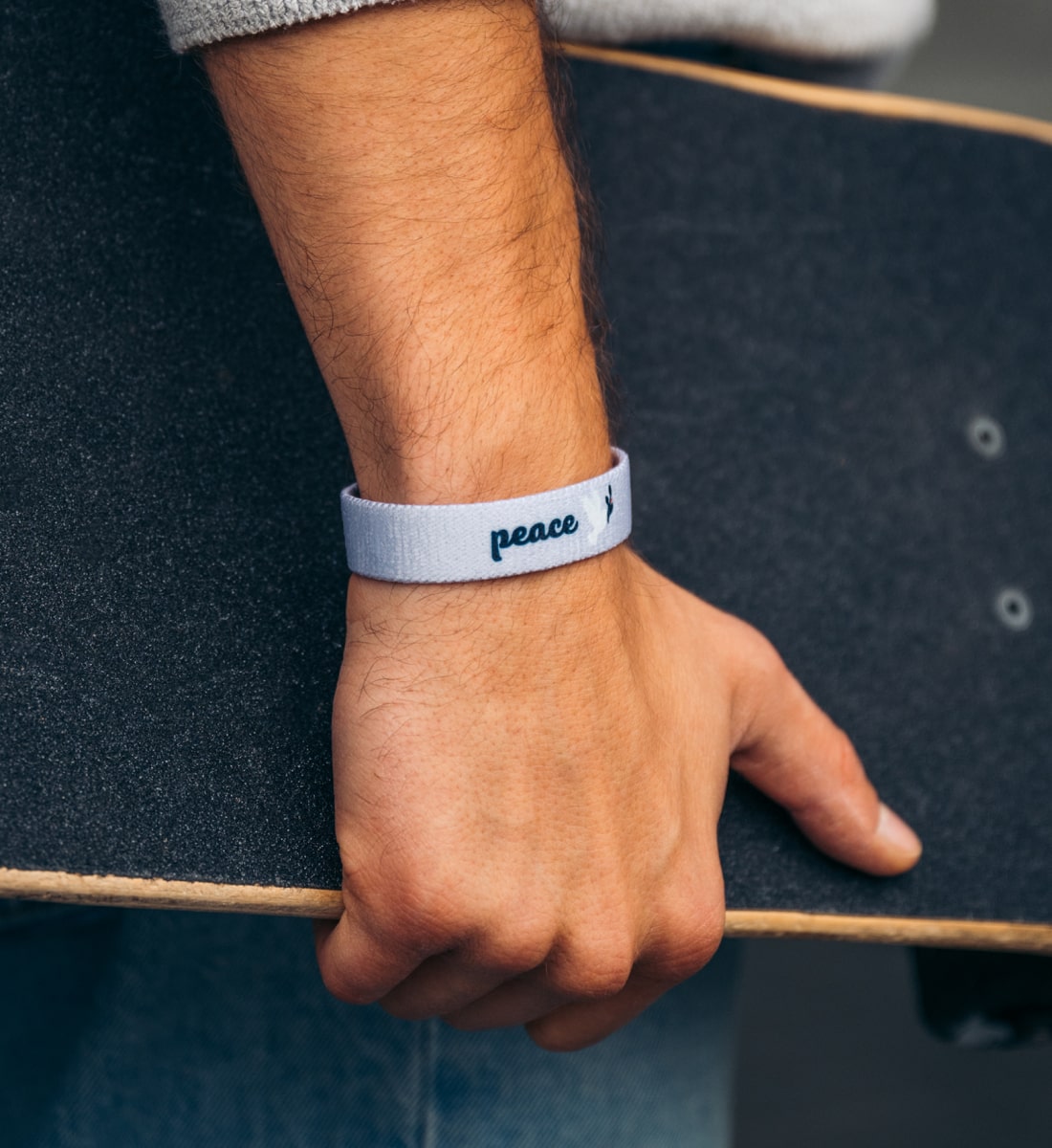Peace Armband in Lavendel mit "peace" Aufschrift und einer weißen Taube getragen von Mann mit Skateboard in der Hand
