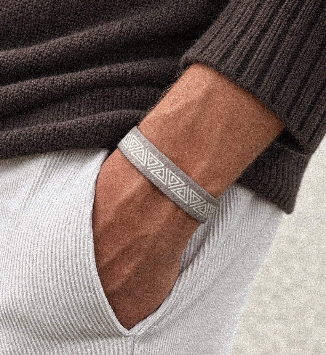Nahaufnahme eines Handgelenks mit einem beigen, elastischen Stoffarmband aus recyceltem Material  – getragen zu braunem Wollpullover und hellen Cord-Shorts als sommerliches Accessoire.