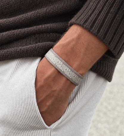 Nahaufnahme eines Handgelenks mit einem beigen, elastischen Stoffarmband aus recyceltem Material  – getragen zu braunem Wollpullover und hellen Cord-Shorts als sommerliches Accessoire.