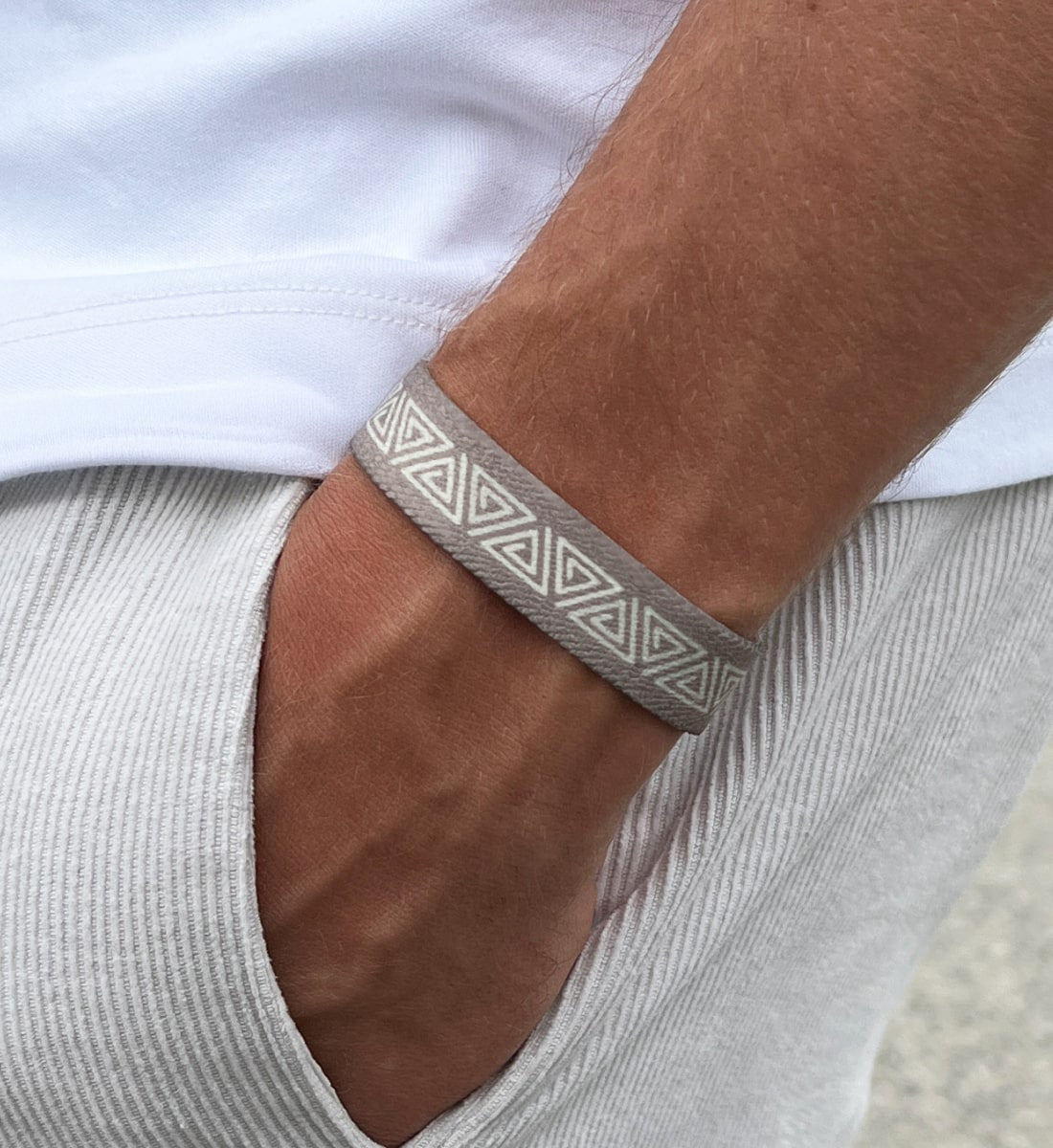 Nahaufnahme eines Handgelenks mit einem beigen, elastischen Stoffarmband aus recyceltem Material  – getragen zu weißem T-Shirt und hellen Cord-Shorts als sommerliches Accessoire.
