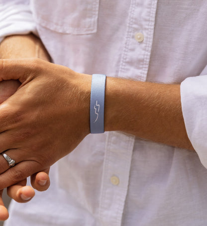 Elastisches Stoff-Armband von Goodbands aus der "airwaves" Kollektion mit Schwingungs-Symbol in grau-blau, am Handgelenk von einem Mann