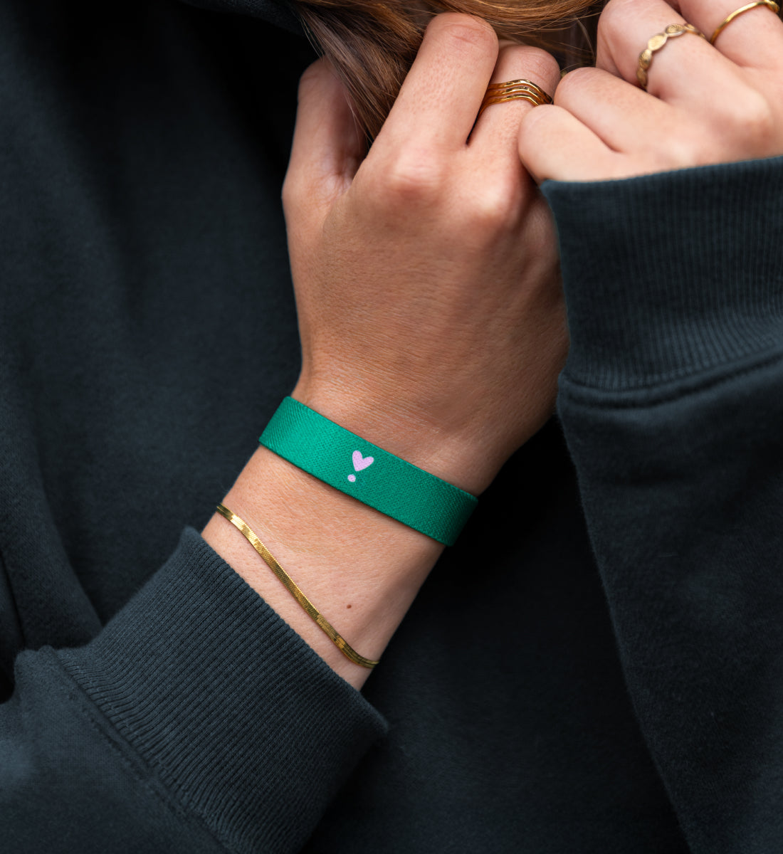 Elastisches Armband von Goodbands aus der "good energy" Kollektion mit Herz-Symbol in pink & grün, am Handgelenk von einer jungen Frau getragen