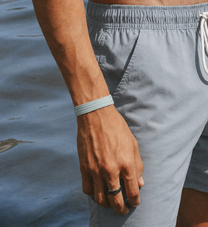 Nahaufnahme eines dünnen, blau-grün gestreiften Stoffarmbands am Handgelenk eines Mannes am Wasser.
